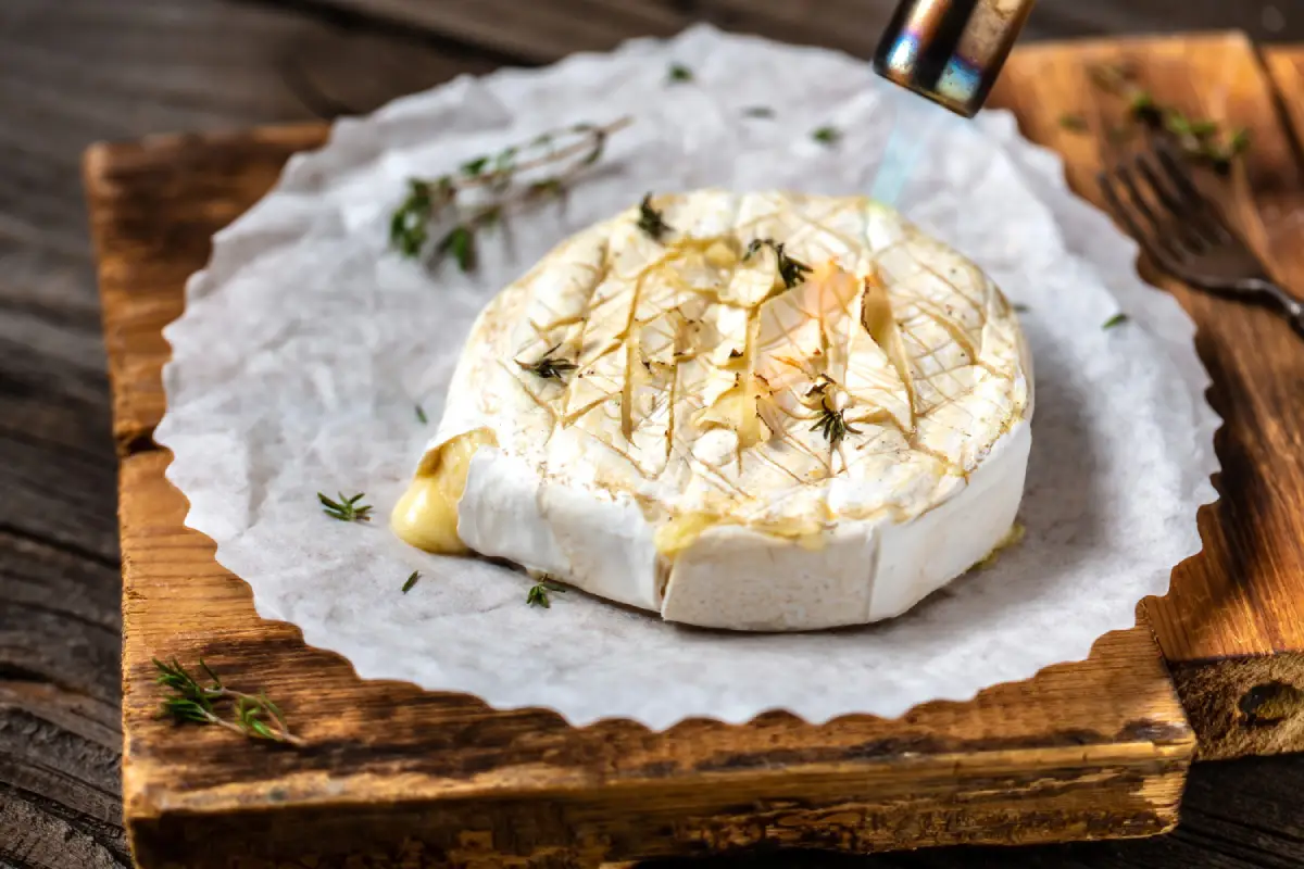 Baked Camembert cheese with thyme on a rustic wooden table.