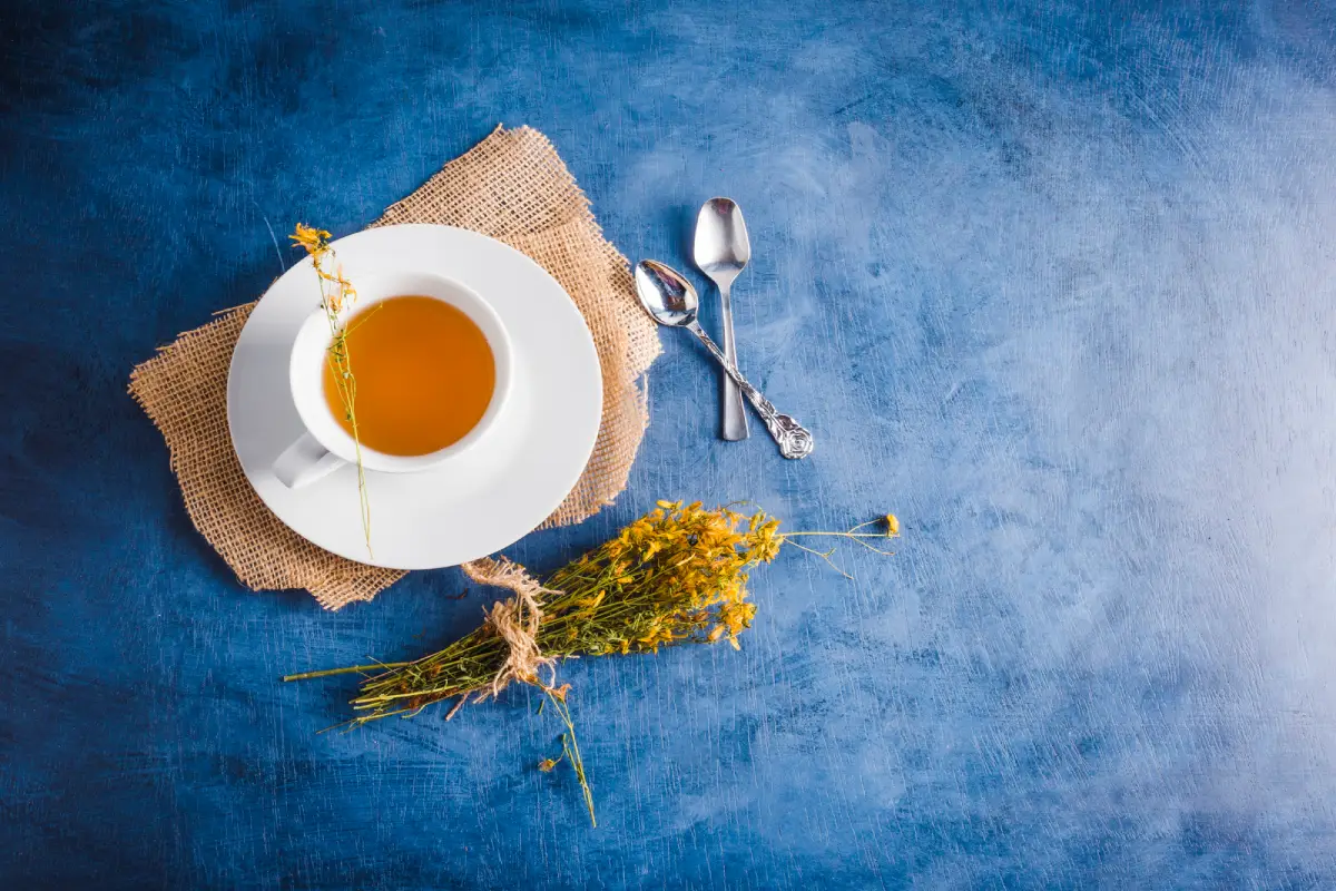 Steaming cup of Earl Grey tea with dried herbs on a blue backdrop