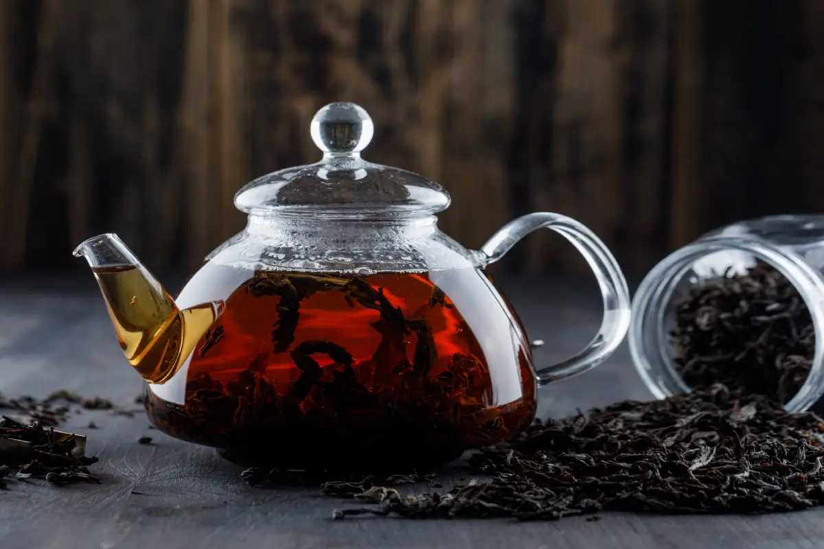 A clear teapot with steeping Earl Grey tea and loose tea leaves on the side.