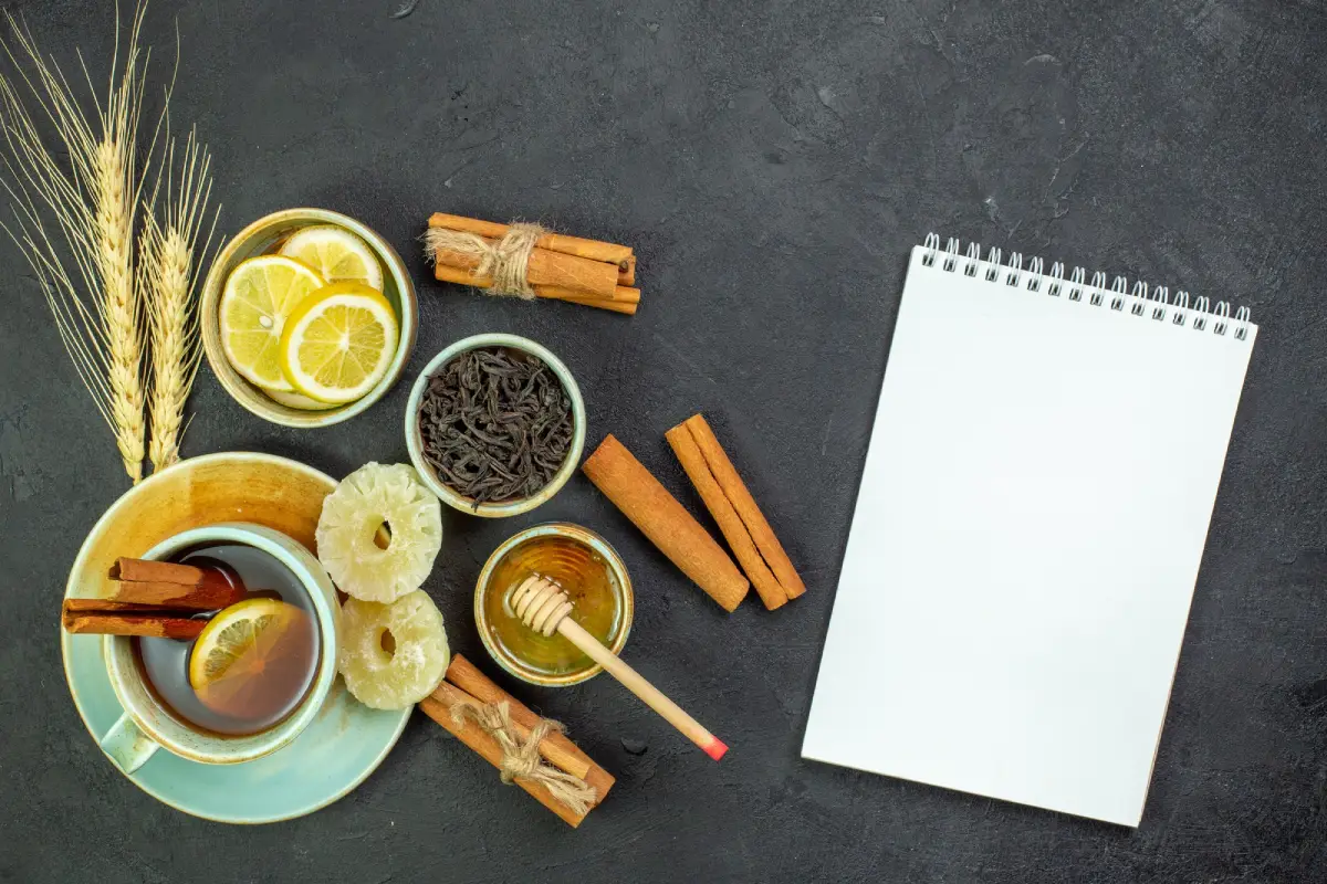 A cup of Earl Grey tea with lemon and honey, surrounded by ingredients and an open notebook.