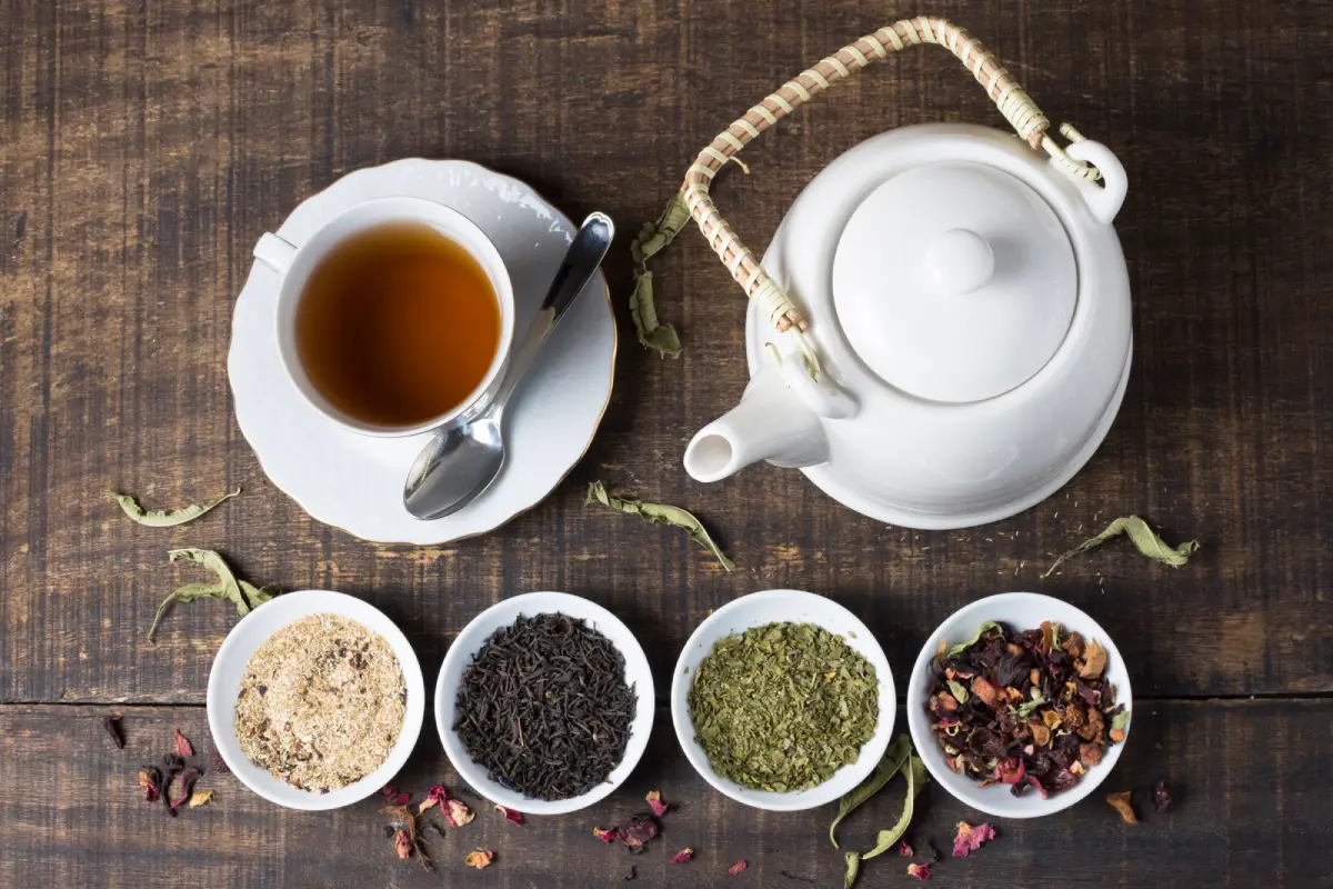 A cup of Earl Grey tea with a selection of other teas and a white teapot on a wooden surface