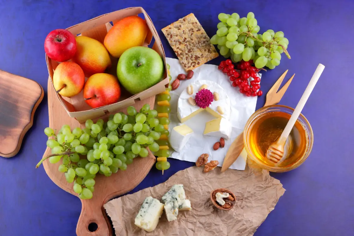 A vibrant display of Camembert cheese with fresh fruits, nuts, and honey on a wooden board.