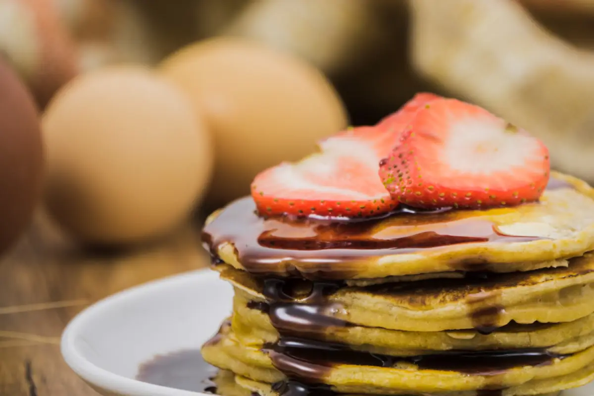 Close-up of mini pancakes stacked with chocolate syrup and fresh strawberry slices on top.