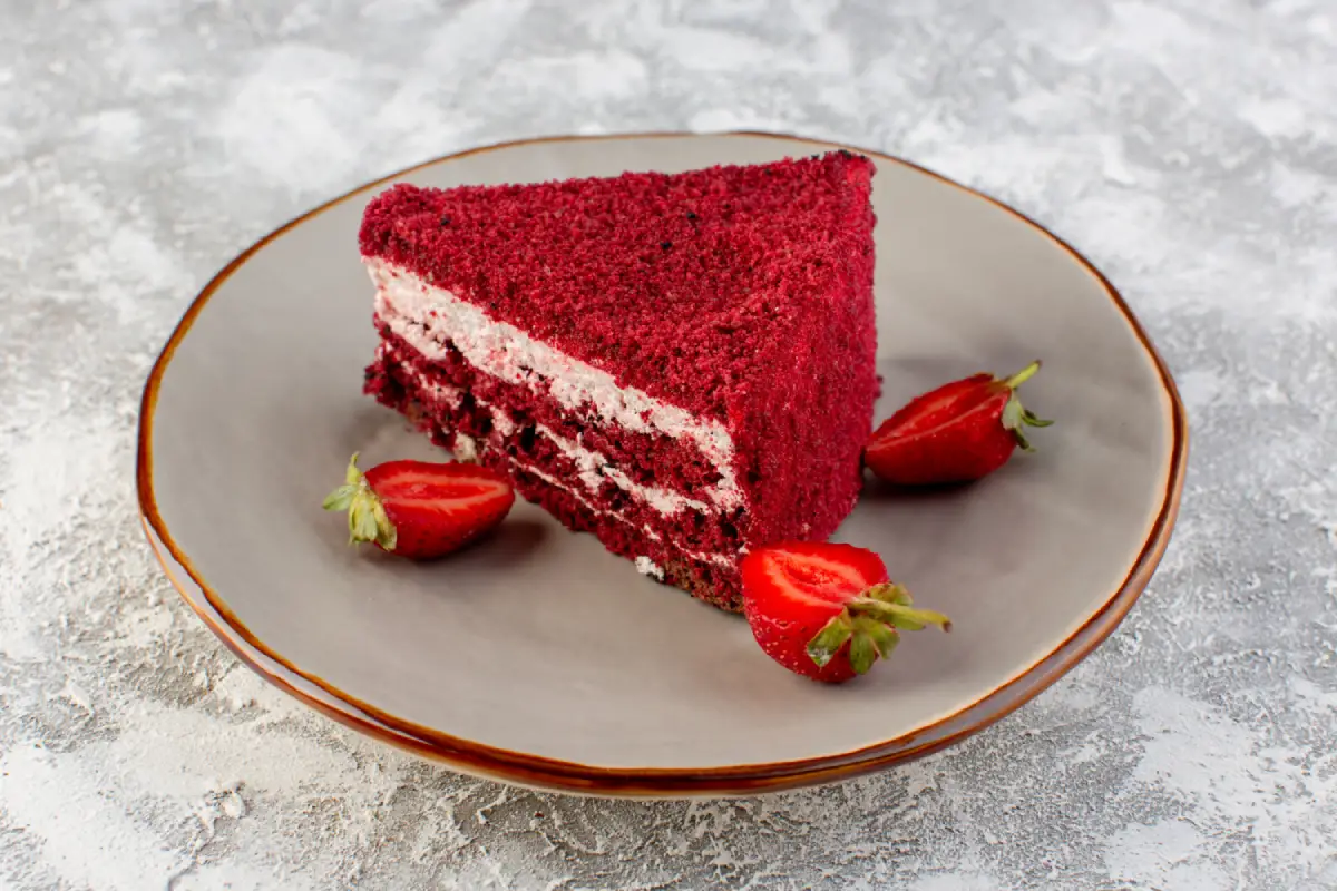 A slice of red velvet cake with strawberry cream filling and fresh strawberries on the side