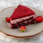 A slice of red velvet strawberry cake on a plate with fresh strawberries