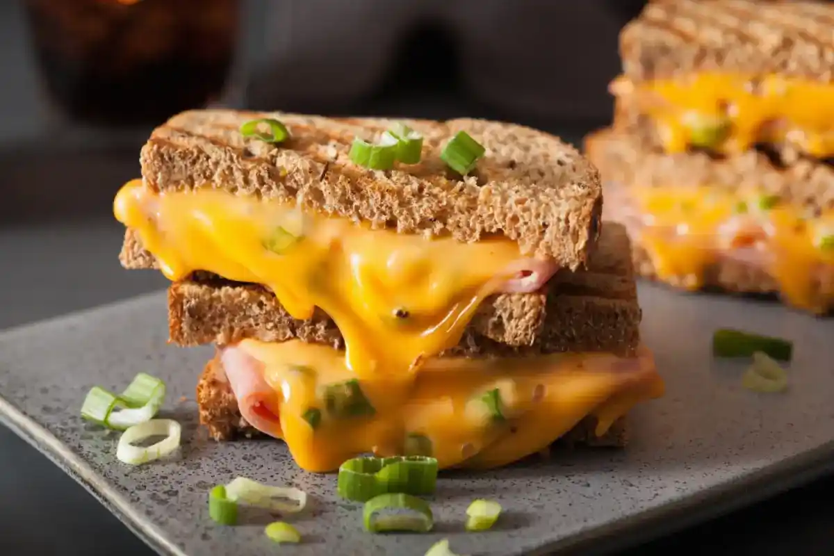 Gooey cheese melting out of a grilled cheese sandwich with ham and green onions.
