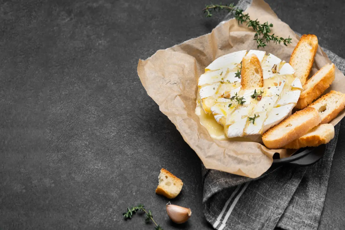 Baked Brie cheese with toasted bread and herbs on a rustic presentation.