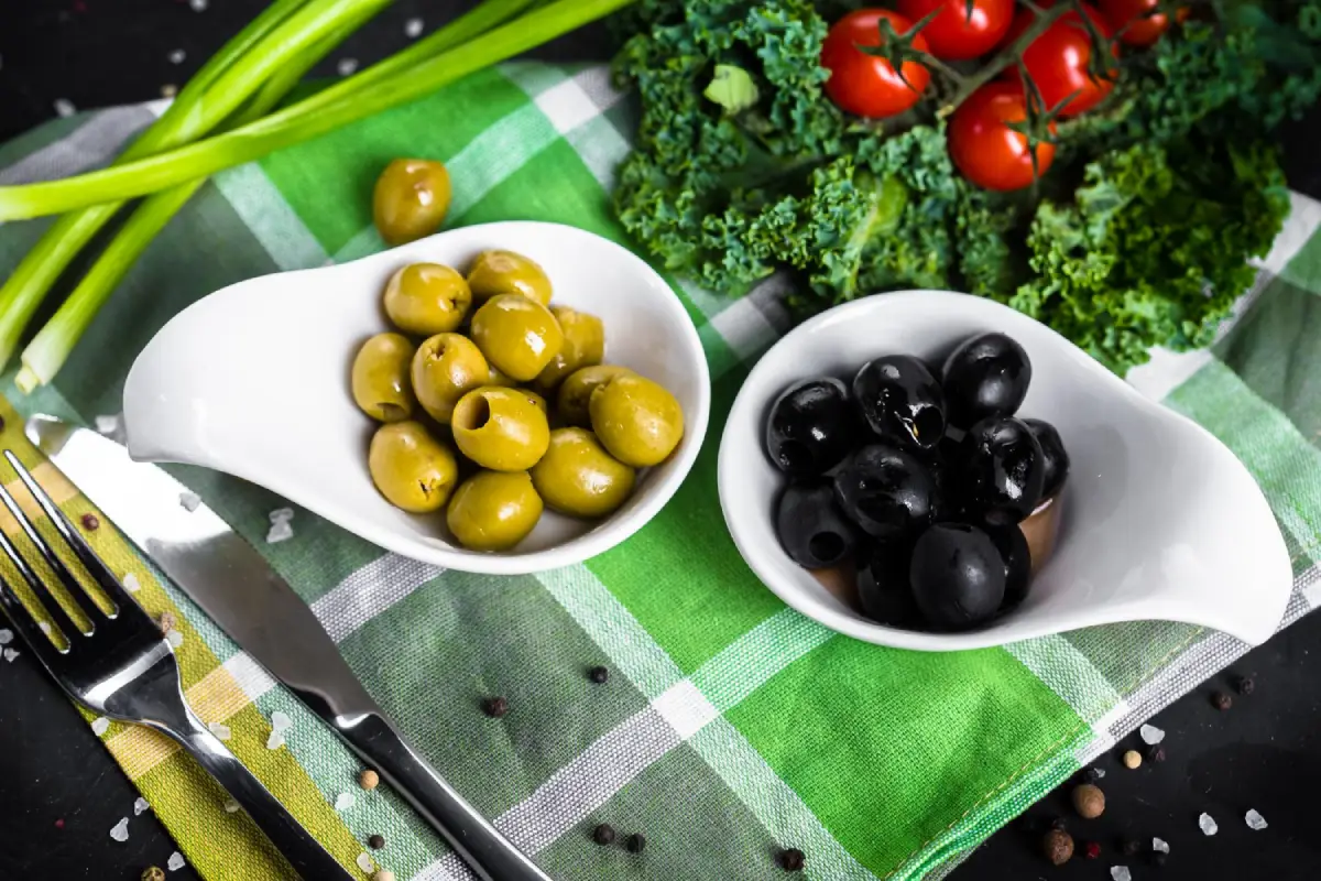 Green and black olives in white bowls on a checkered napkin, ready to be added to a healthy meal.