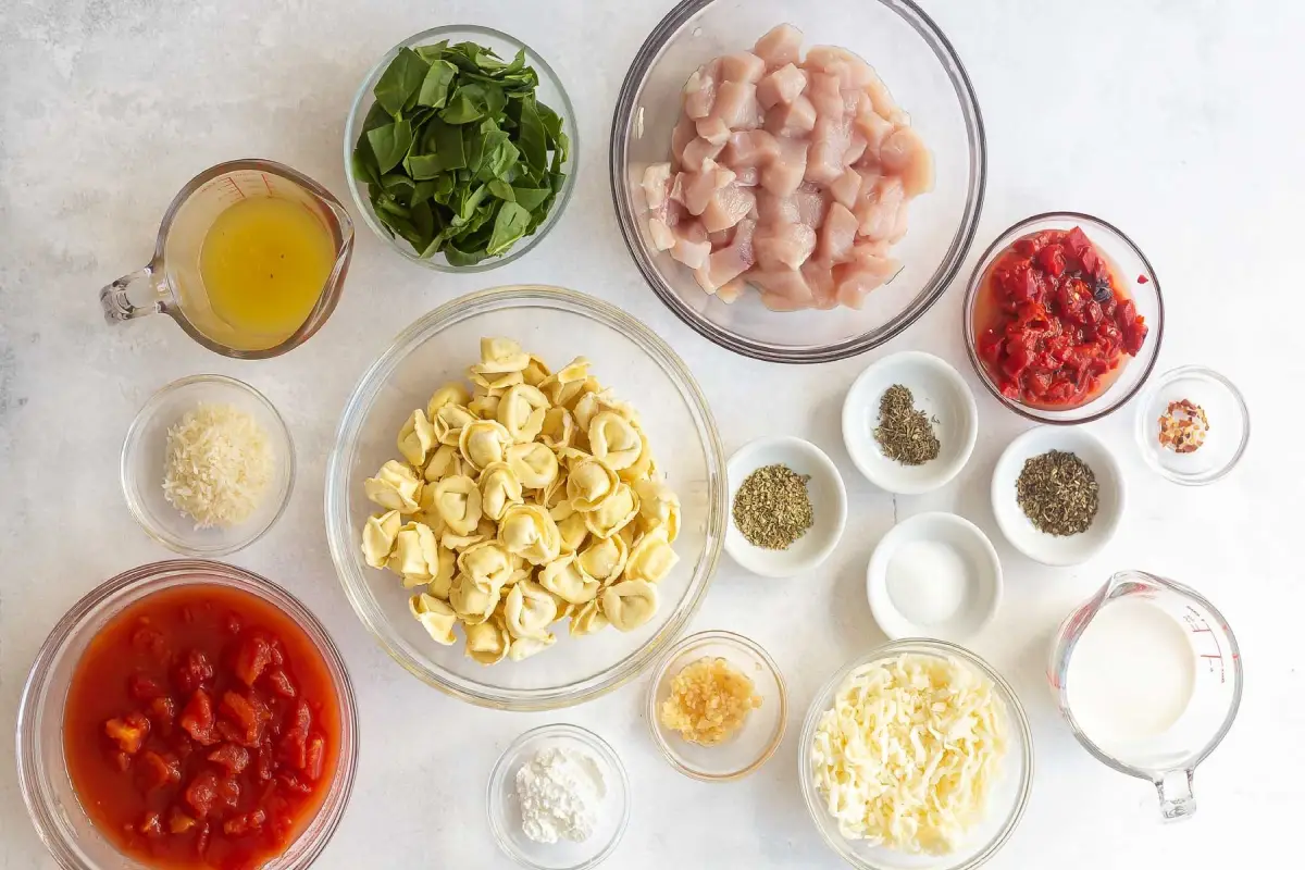 Ingredients laid out for chicken tortellini including fresh spinach, diced chicken, and tortellini pasta.