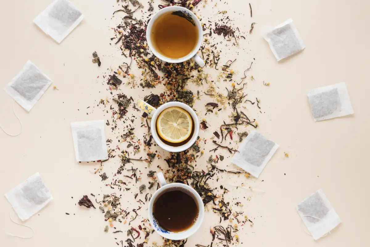 Two cups of Earl Grey tea surrounded by loose tea leaves and multiple tea bags on a beige surface.