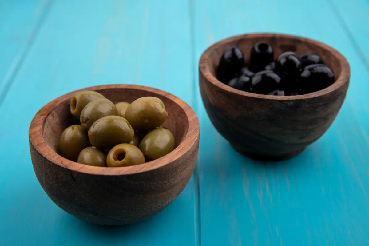Bowls of green and black olives on a turquoise background illustrating a nutritional comparison