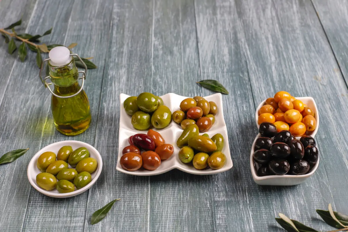 A selection of green, Kalamata, and black olives with olive oil on a wooden surface.