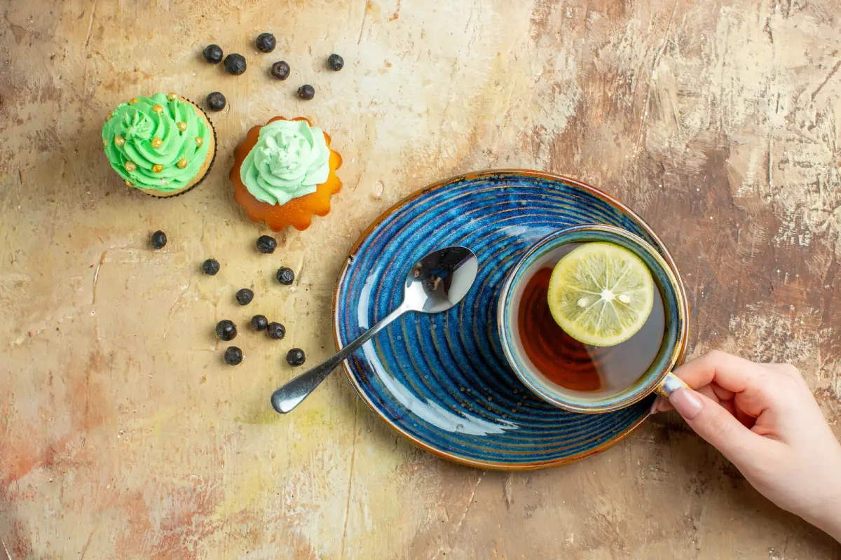 A cup of tea with lemon, spoon, and cupcakes on a colorful saucer.