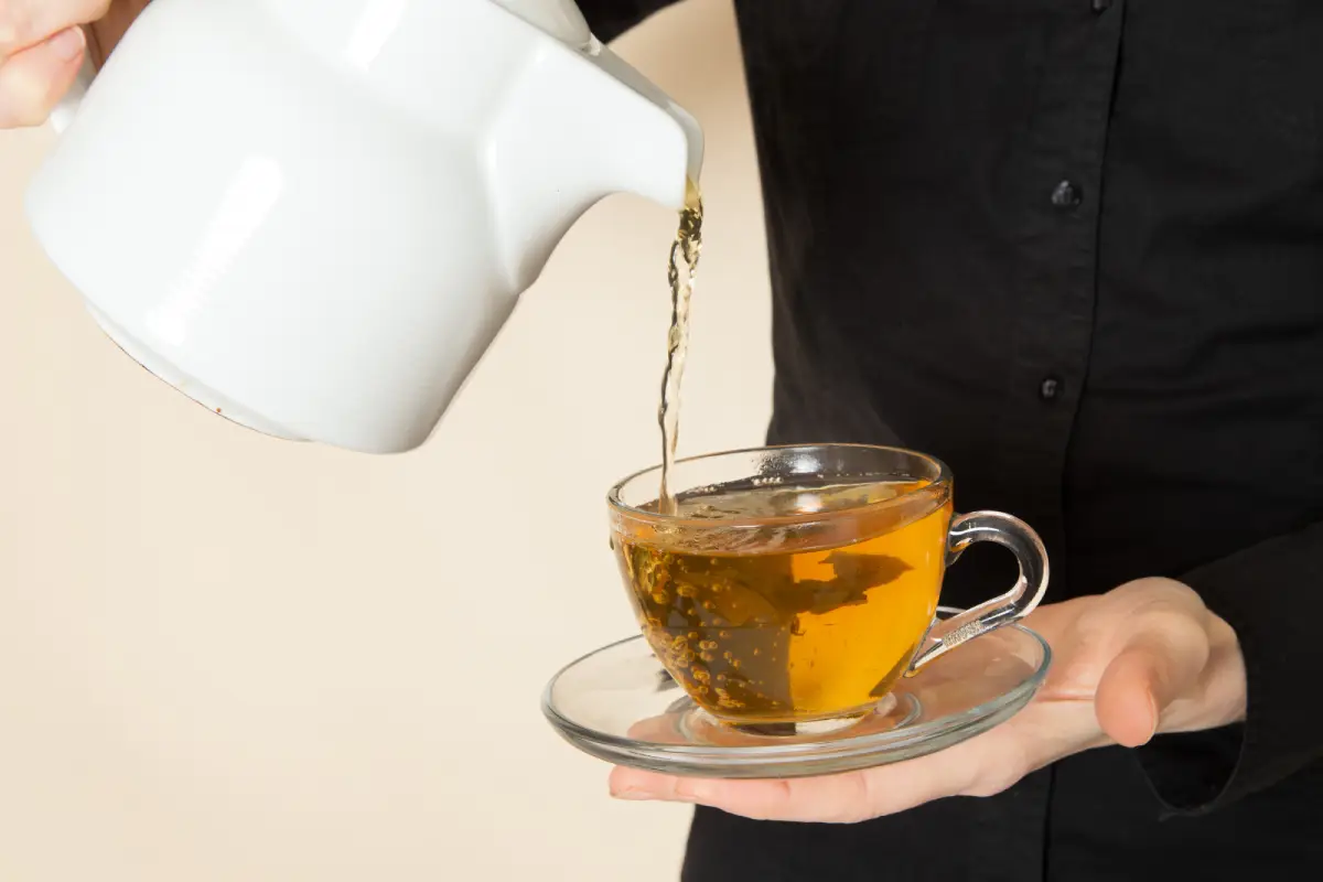 Pouring hot Earl Grey tea into a clear cup held by a person in a black shirt