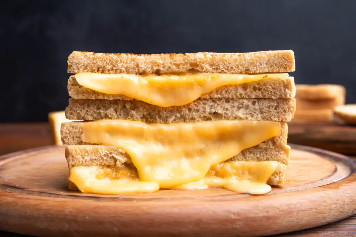 Close-up of a grilled cheese sandwich with perfectly melted cheese on a wooden cutting board.