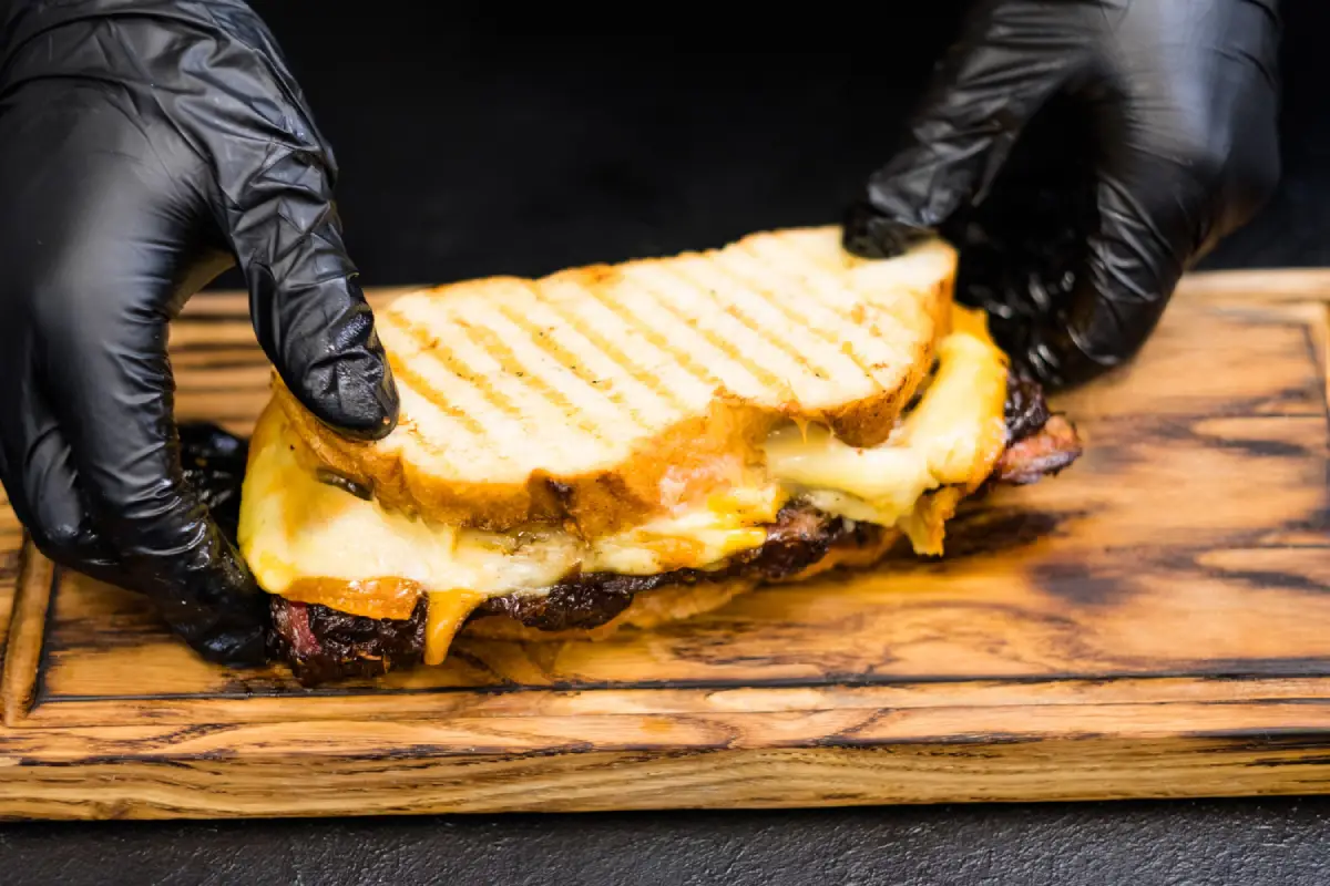 A chef preparing a grilled cheese sandwich with smoked beef brisket.