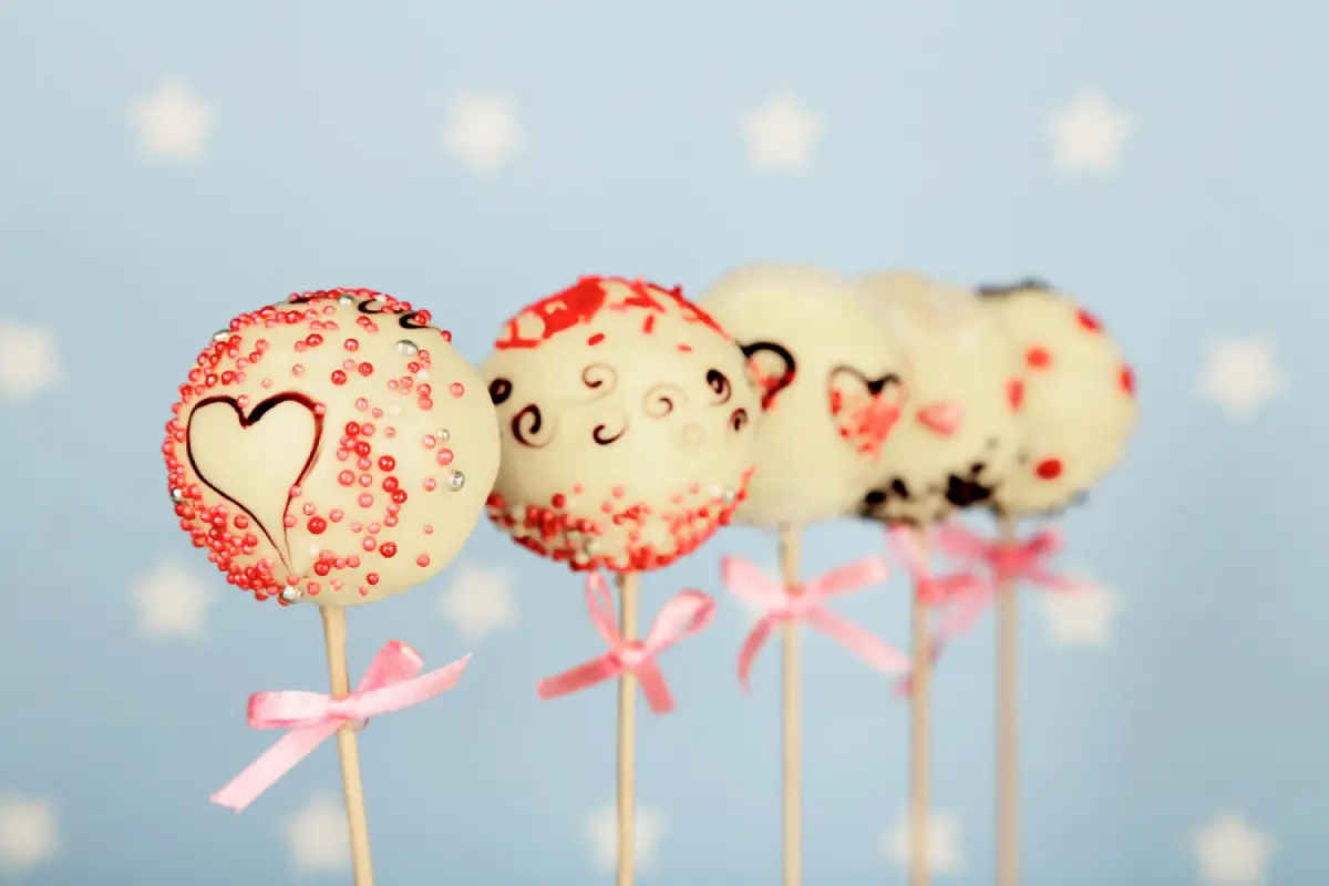 Valentine-themed cake pops adorned with hearts and sprinkles on a blue background