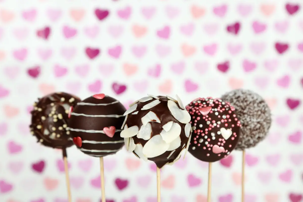 Assorted Valentine's Day themed cake pops in front of a heart-patterned background