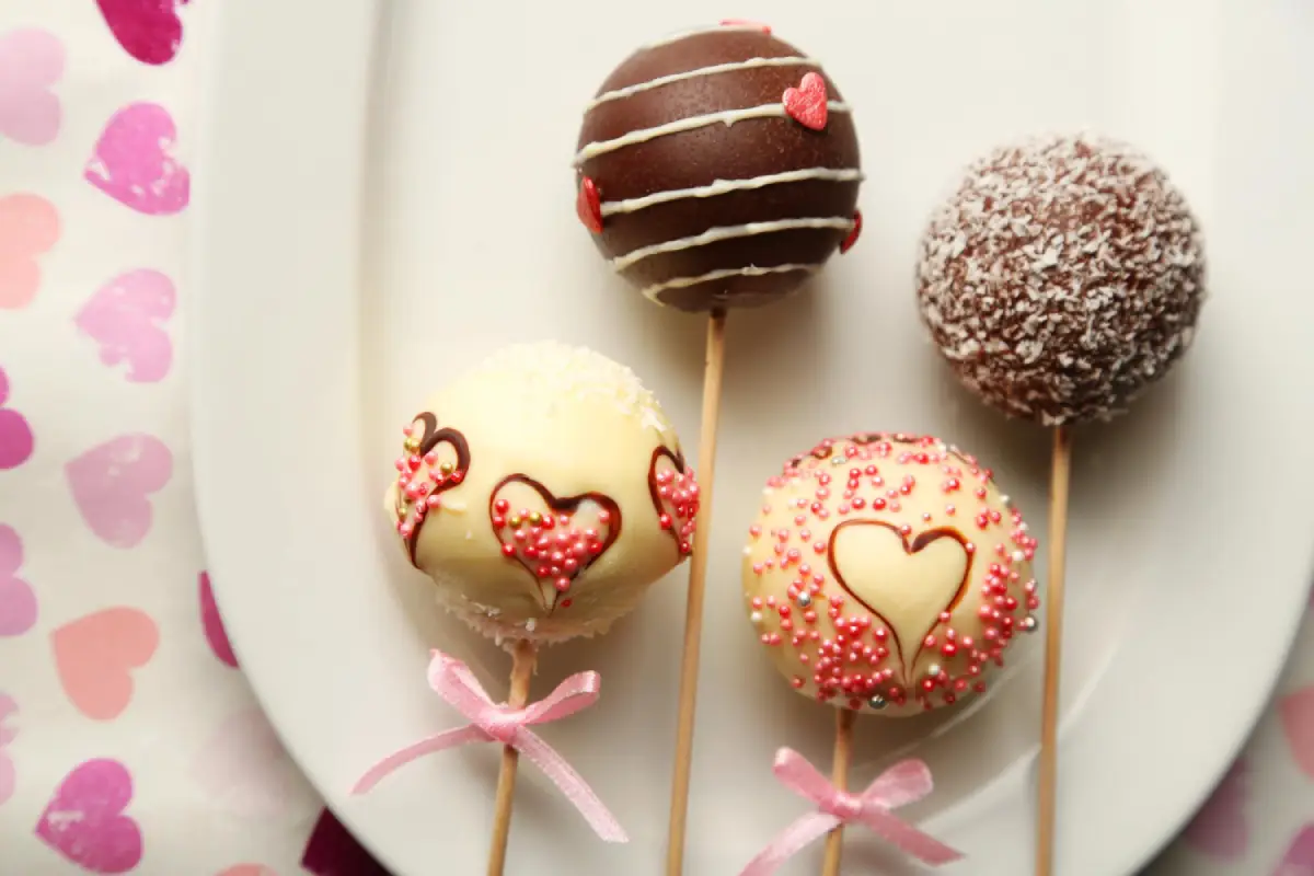 Assorted Valentine-themed cake pops adorned with hearts and sprinkles on a white plate
