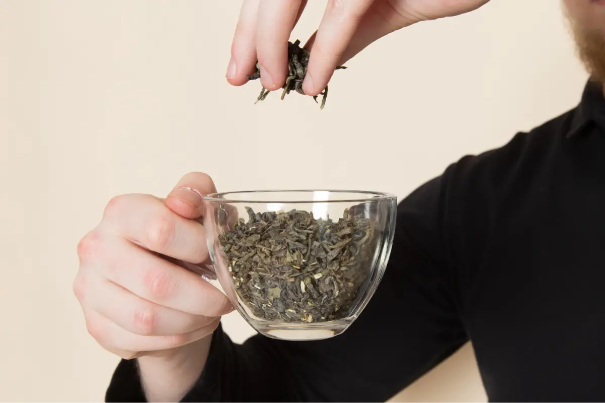 A person holding a clear glass cup filled with loose Earl Grey tea leaves.