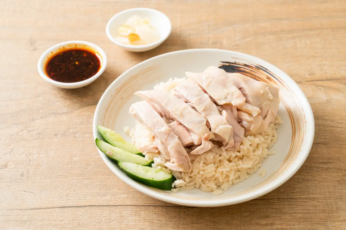 Hainanese Chicken Rice accompanied by chili and garlic sauce on a wooden table.