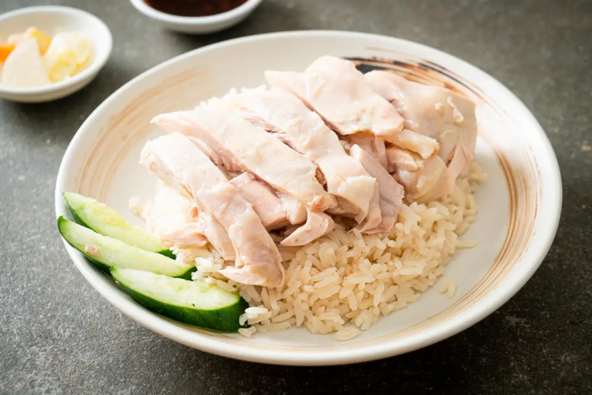 A simple plate of Hainanese Chicken Rice served with cucumber slices and condiments.