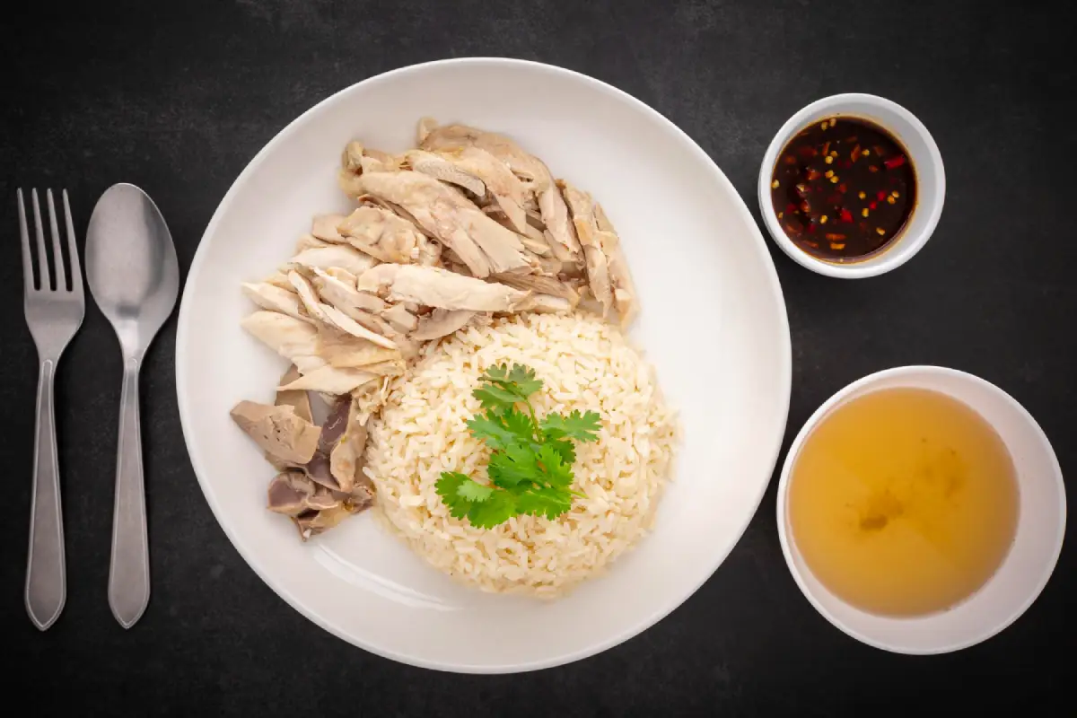 Overhead view of a plate of Classic Hainanese Chicken Rice with soup and chili sauce.