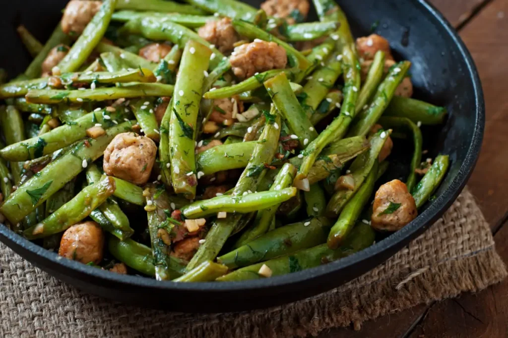 A close-up of a skillet filled with sautéed green beans and diced herbs.