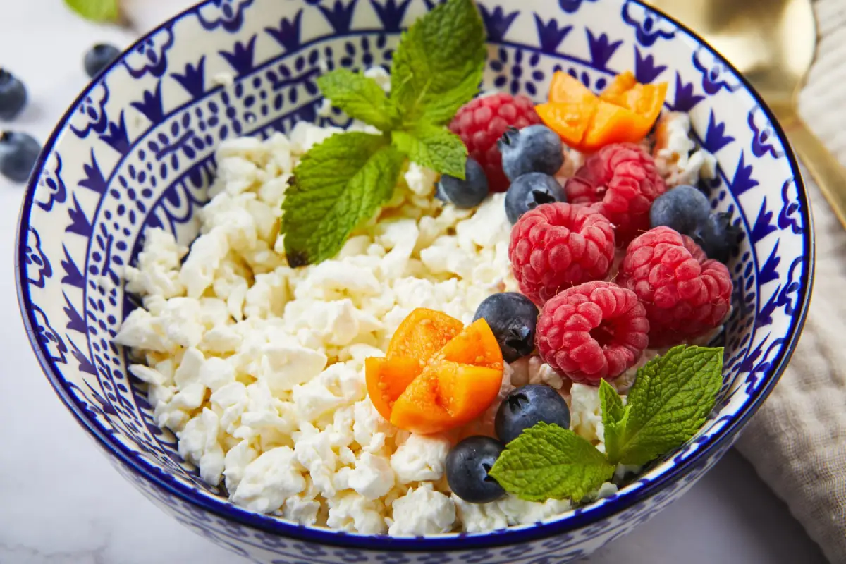 A colorful bowl of cottage cheese topped with various fresh berries and mint leaves.