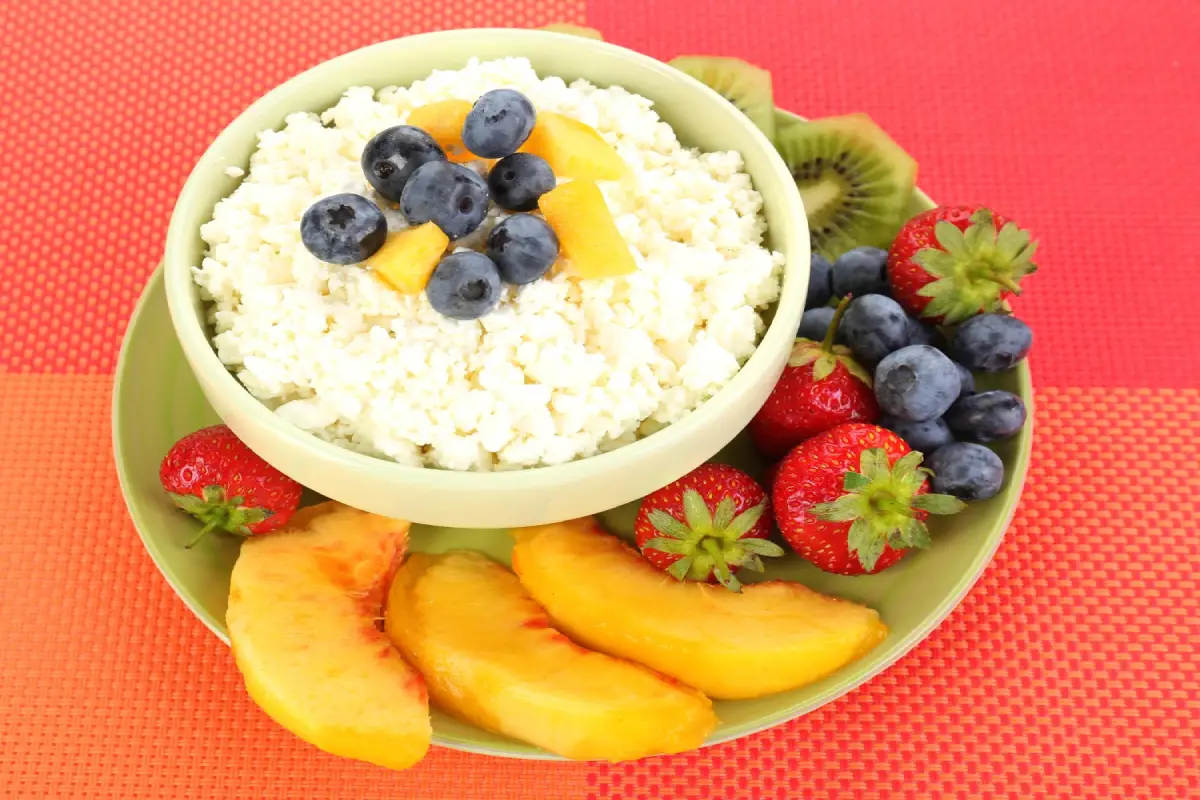 A bowl of cottage cheese with blueberries and peaches on a colorful tablecloth.