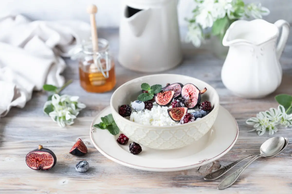 A bowl of cottage cheese topped with figs and mixed berries, on a rustic table setting.