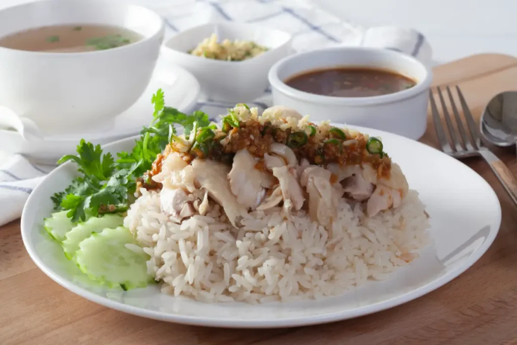 A plate of Malaysian Hainanese Chicken Rice with soup and sauces on the side.