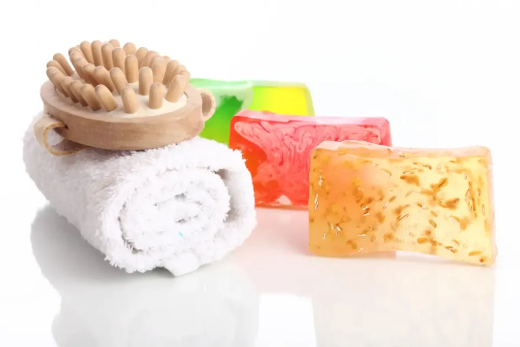 Colorful jelly soaps with a massaging brush on top of a rolled towel.