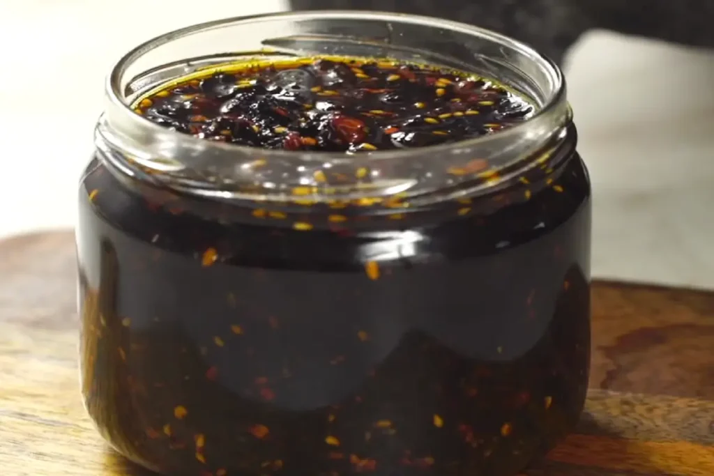A jar filled with dark, rich salsa macha on a wooden surface.