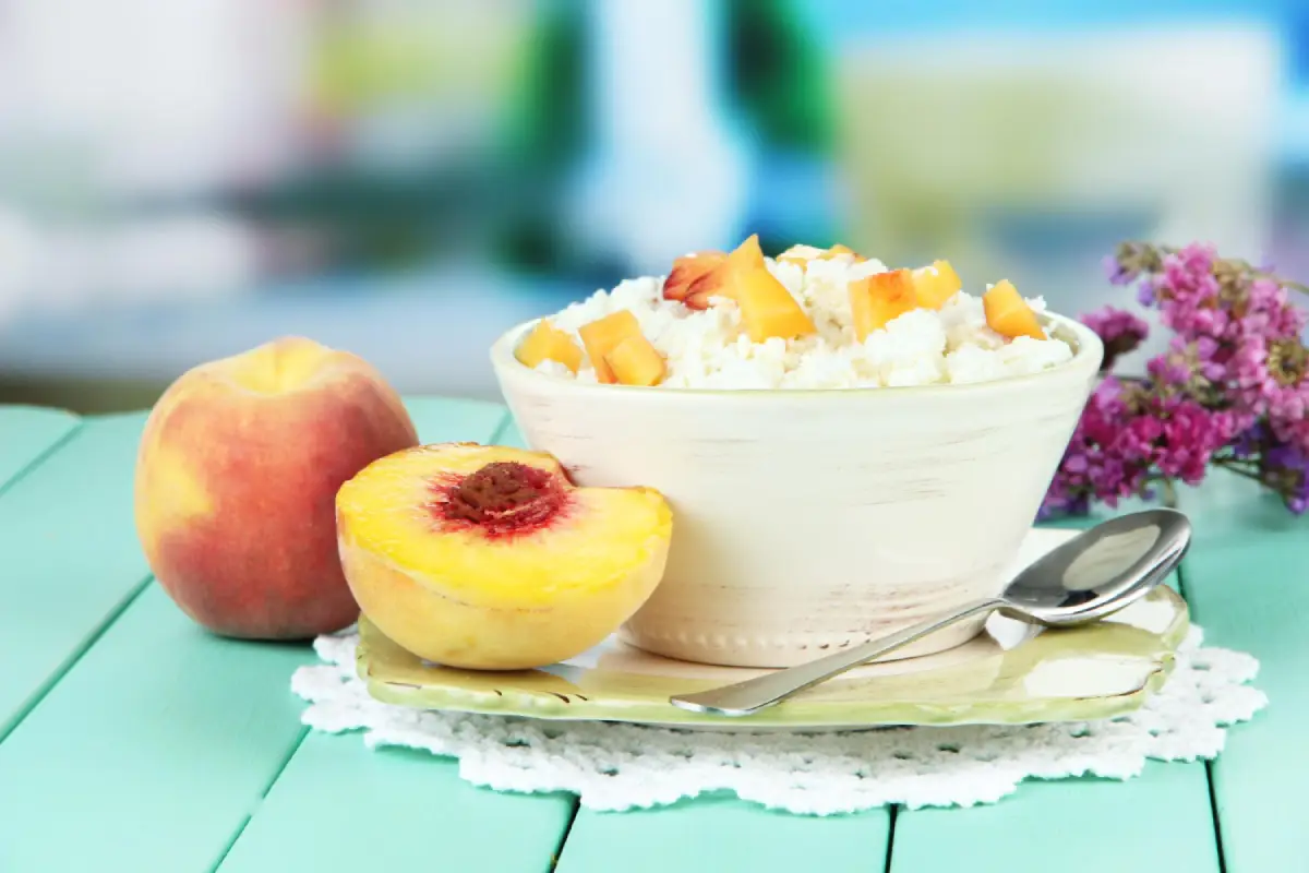 A bowl of cottage cheese topped with fresh peach slices on a turquoise wooden table.