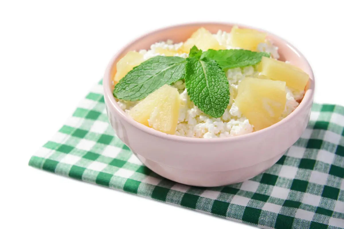 A bowl of cottage cheese with pineapple chunks and mint on a checkered napkin.