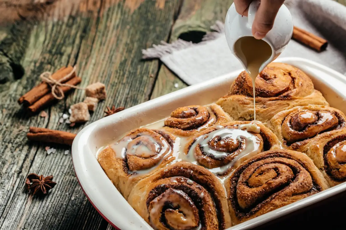 Pouring icing onto warm cinnamon rolls straight from the oven.