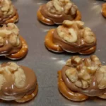 Homemade Rolo Pretzel Bites with nuts on a baking sheet.