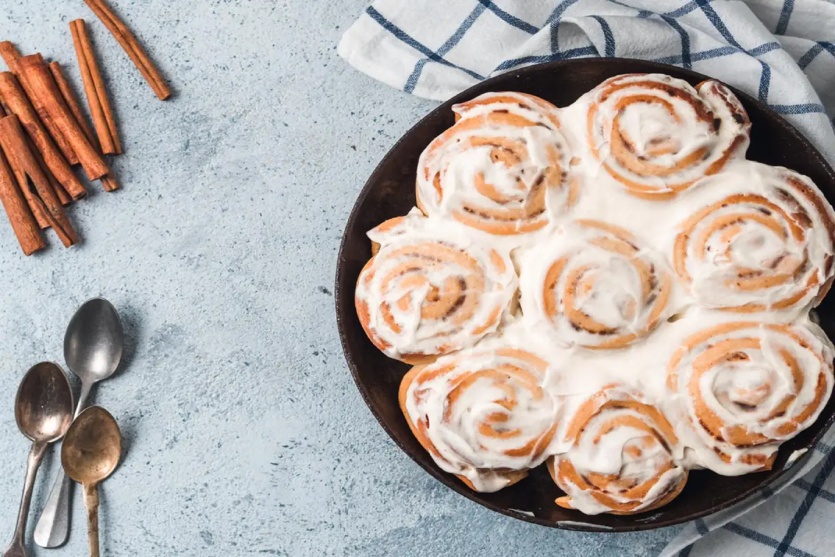  Fresh cinnamon rolls with icing in a skillet, cinnamon sticks on the side.