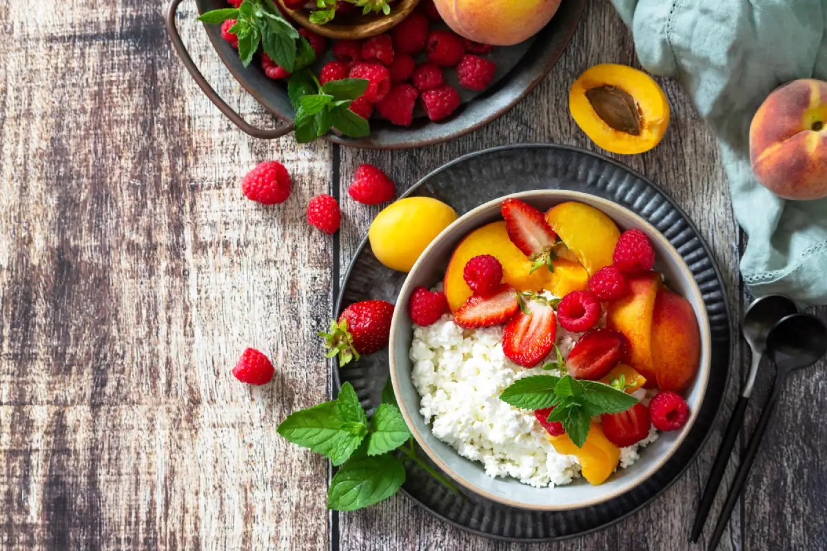 A rustic bowl of cottage cheese garnished with strawberries, peaches, and raspberries.