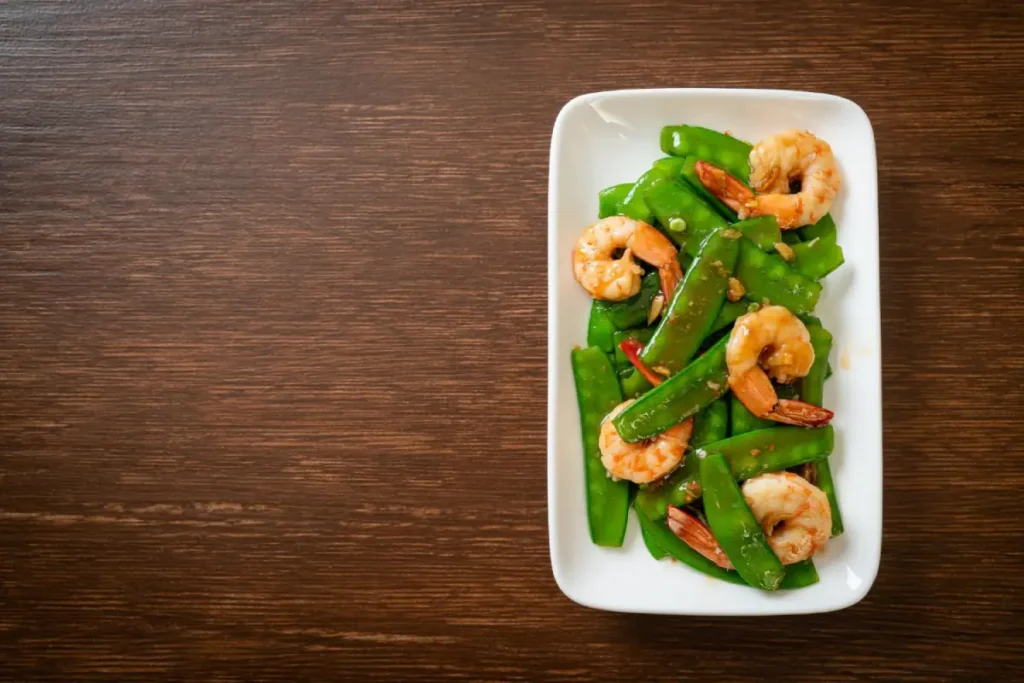 A delectable serving of stir-fried green peas with shrimp on a white plate.