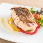 A succulent grilled snapper steak on a bed of bell peppers with a side salad.