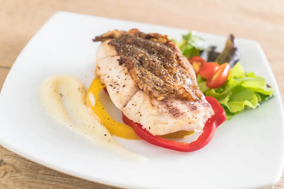 A succulent grilled snapper steak on a bed of bell peppers with a side salad.
